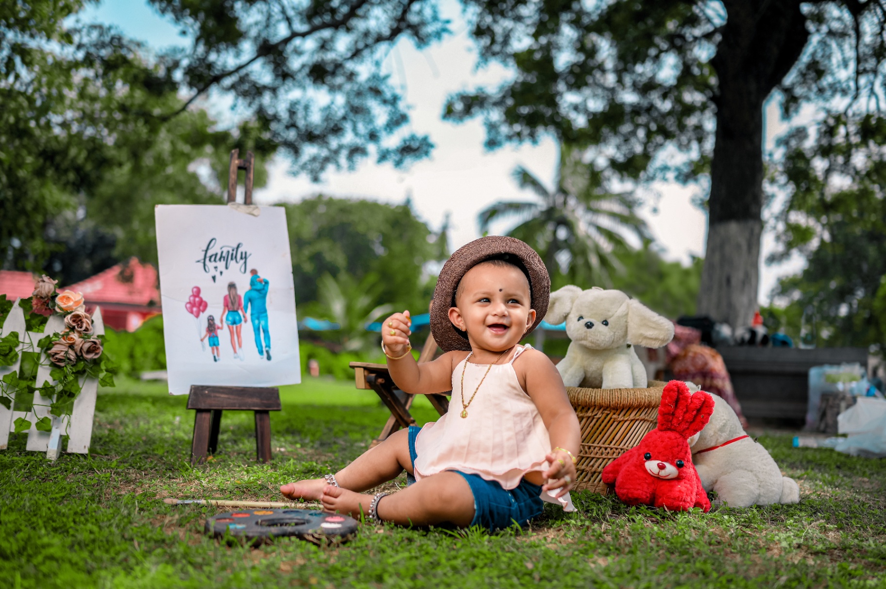 Smiling baby outdoors beside toys and family-themed props during a milestone session