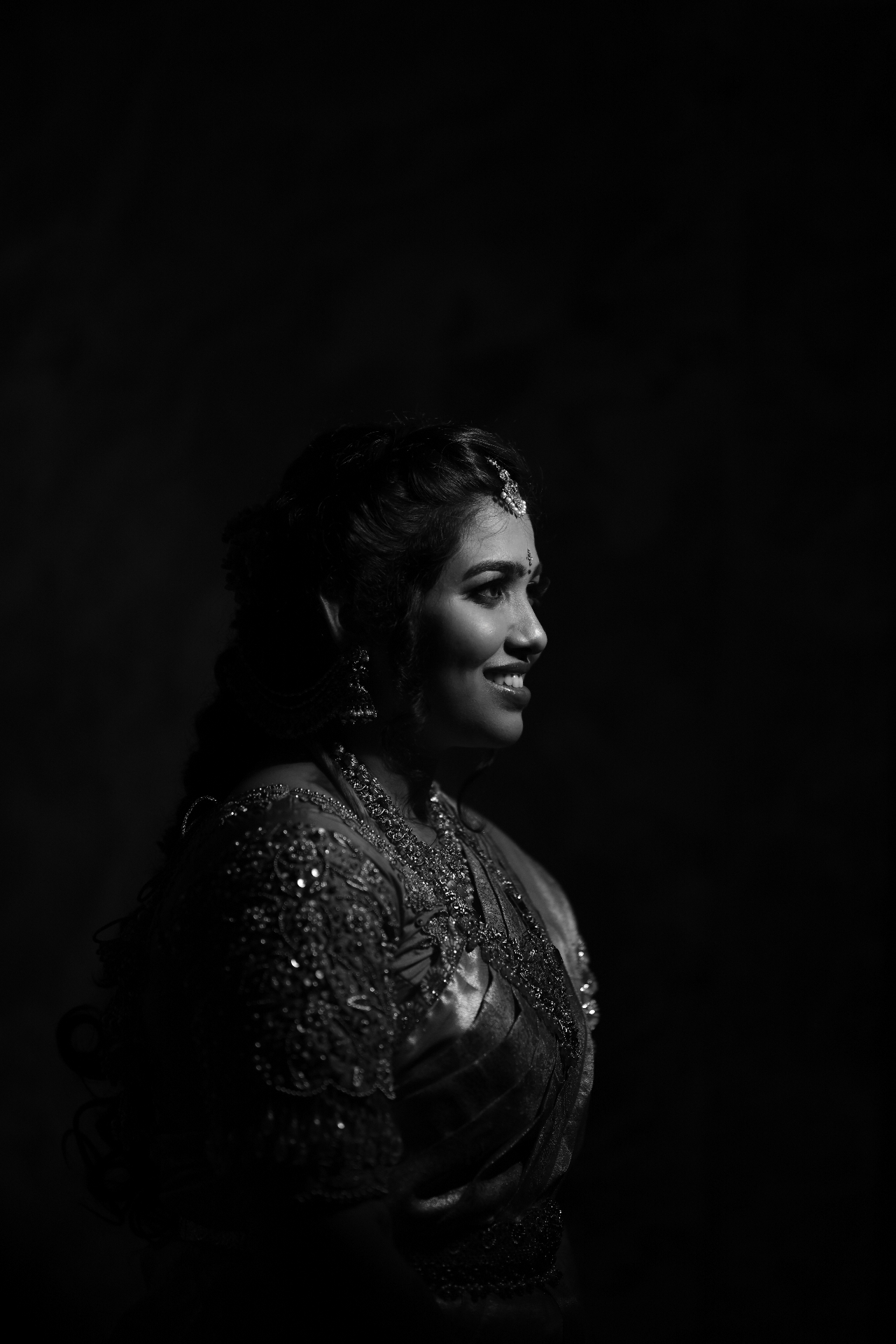 Black and white side profile of a smiling bride lit against a dark backdrop