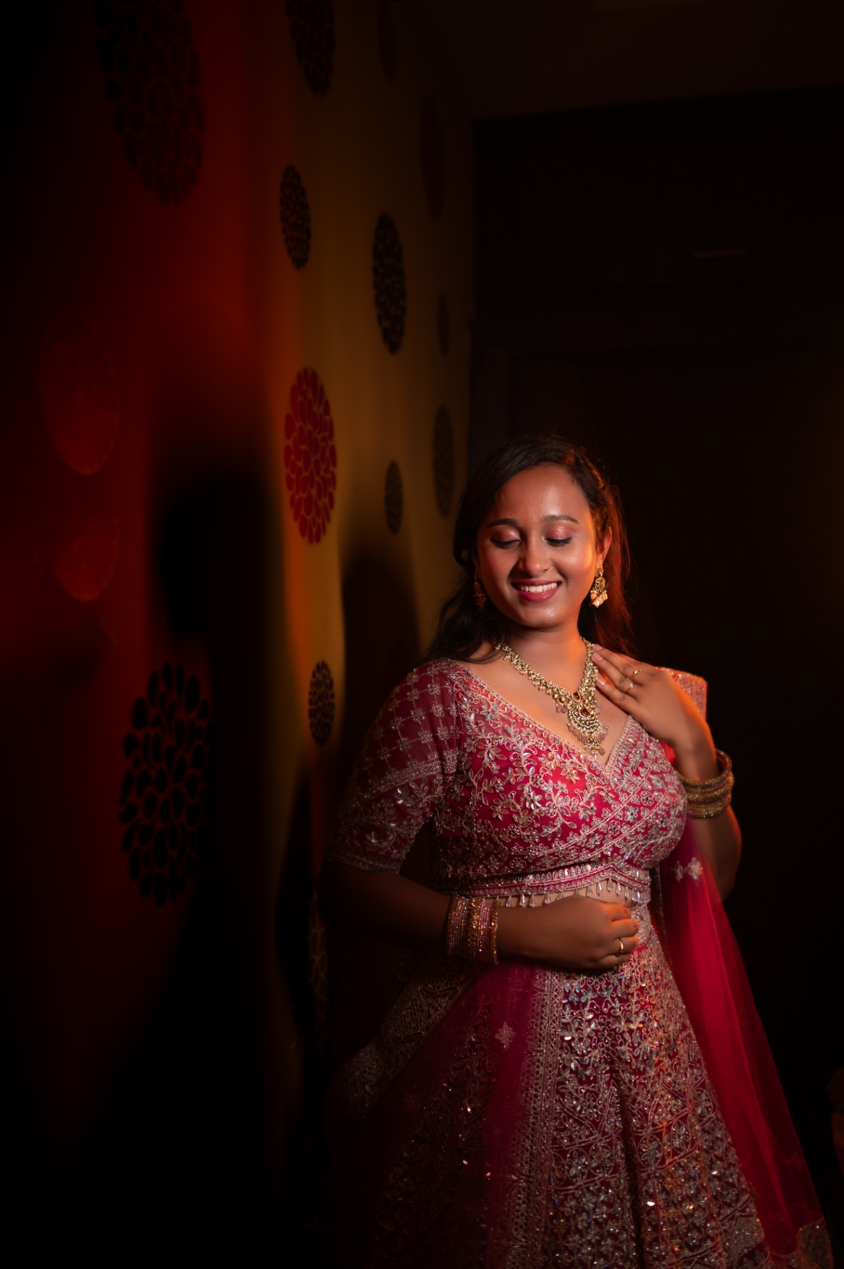 Bride in a pink embellished lehenga lit with warm dramatic light indoors