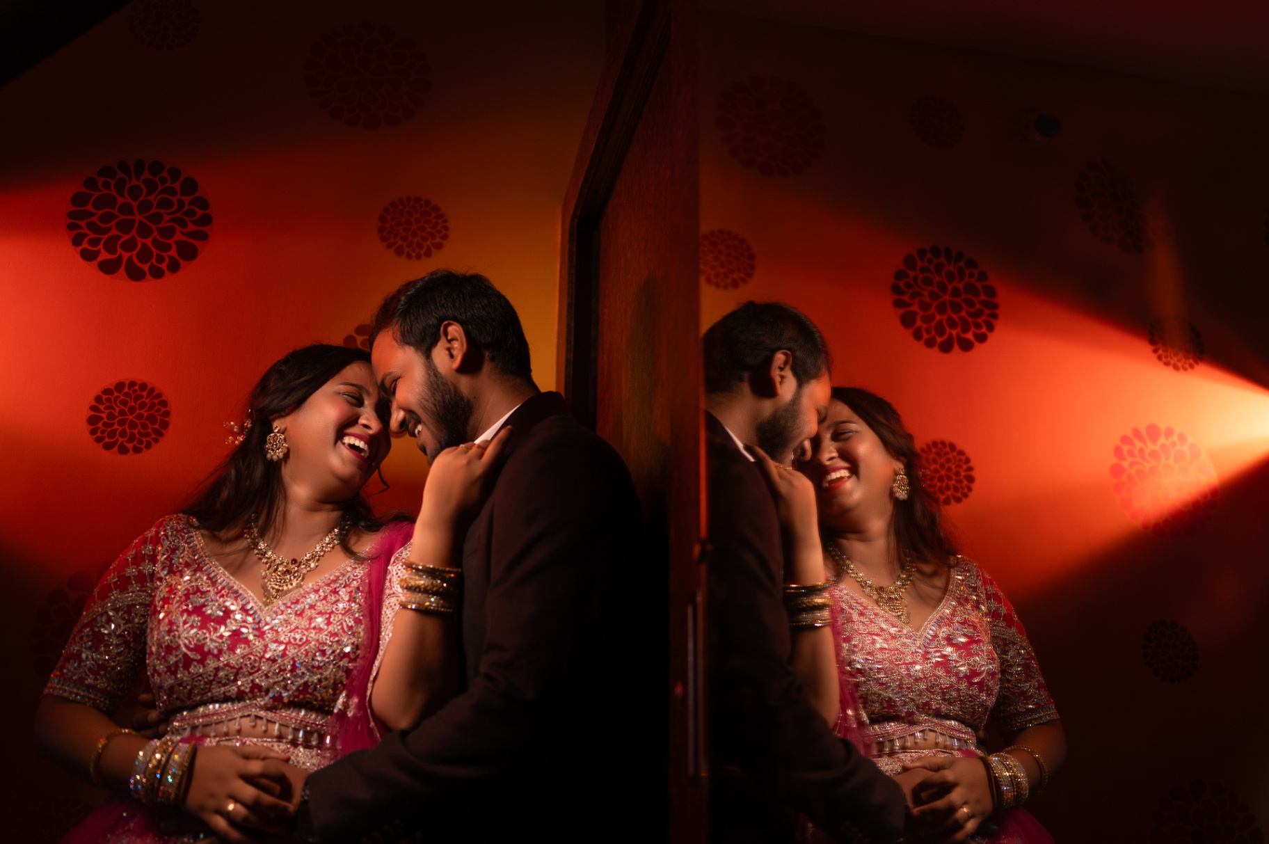 Couple laughing together beside a mirror in warm evening light