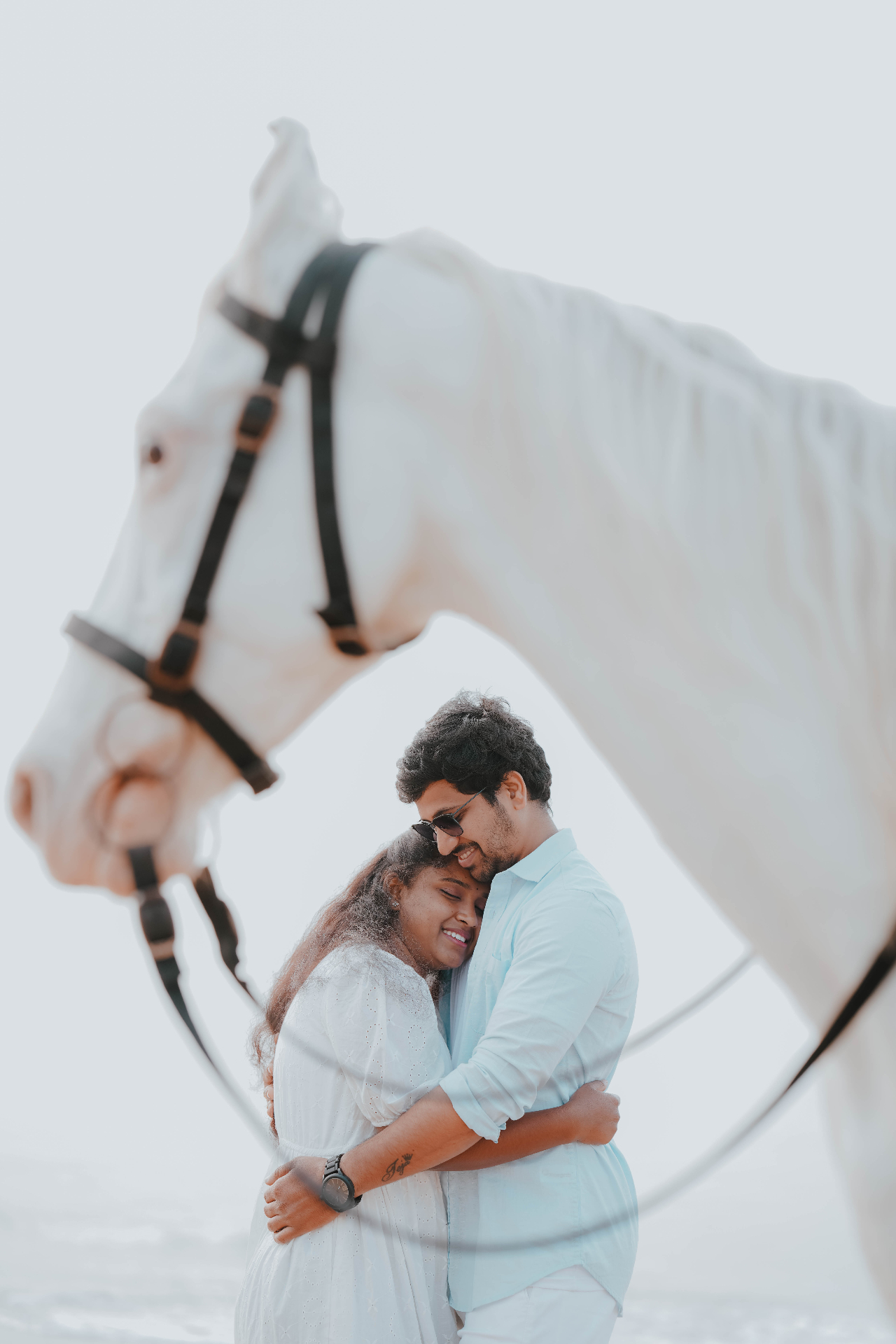 Couple embracing on the beach framed under the neck of a white horse