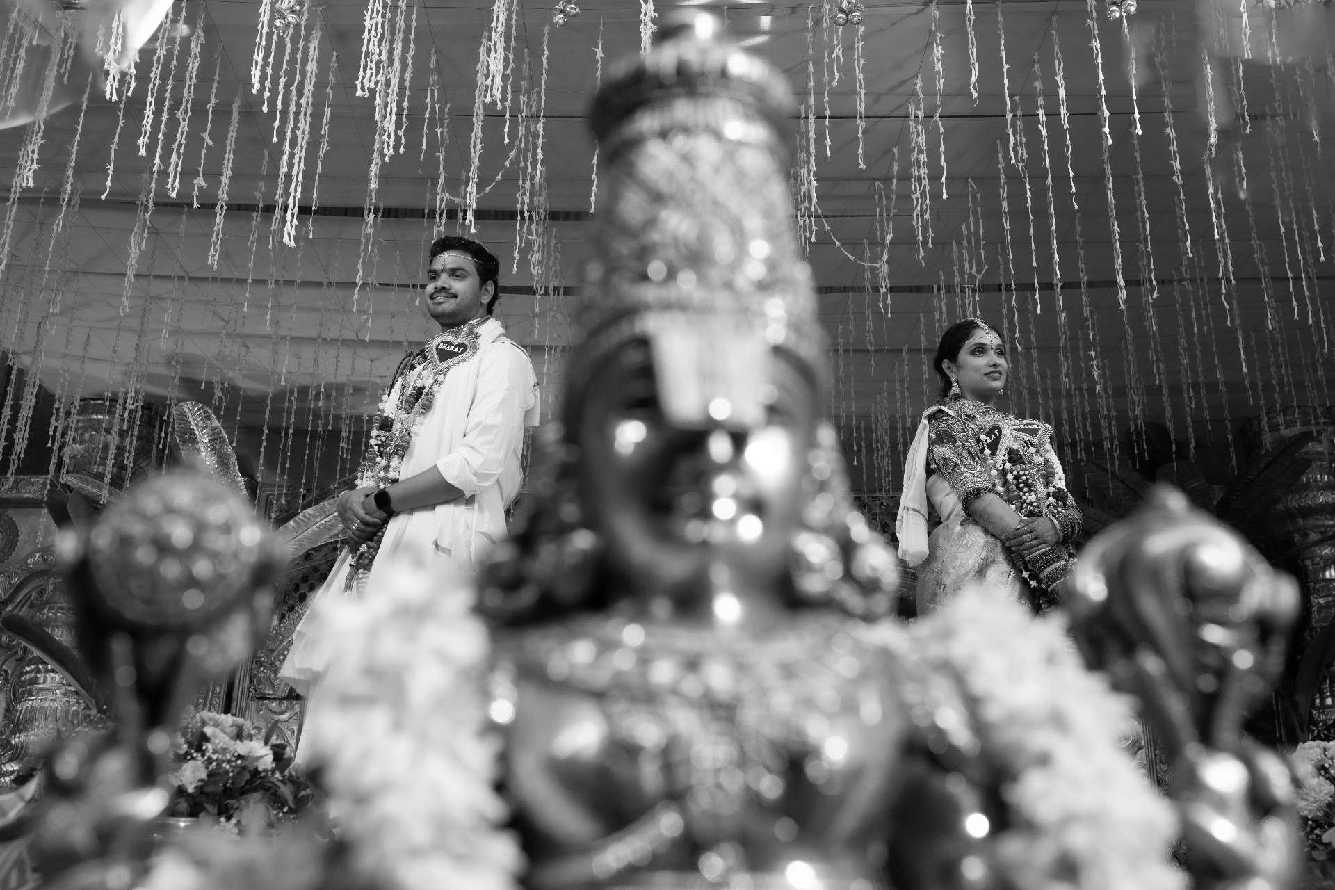 Bride and groom framed behind a blurred sacred statue in a black and white wedding portrait