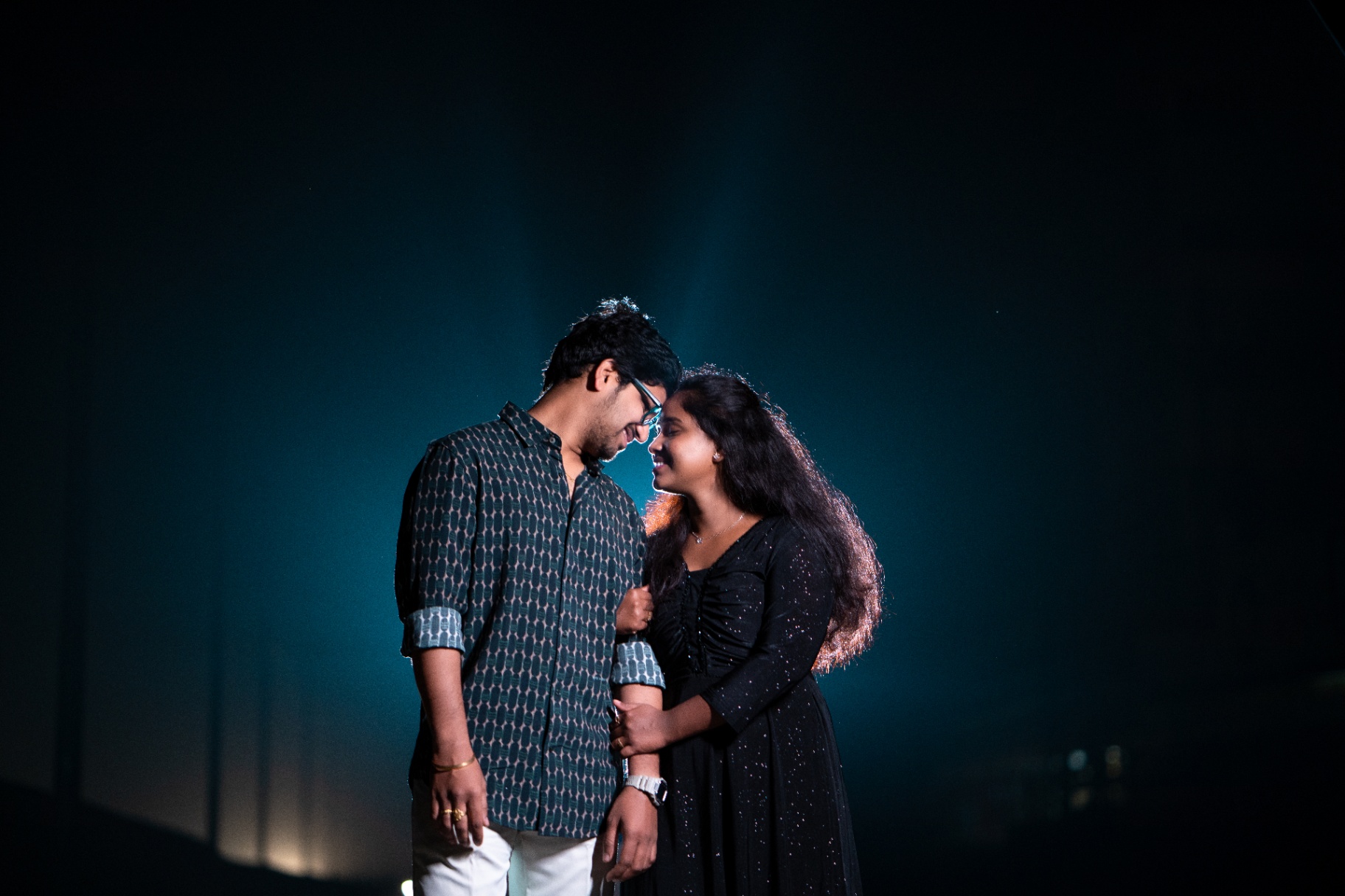 Couple sharing a smile under a dramatic teal spotlight in a night shoot