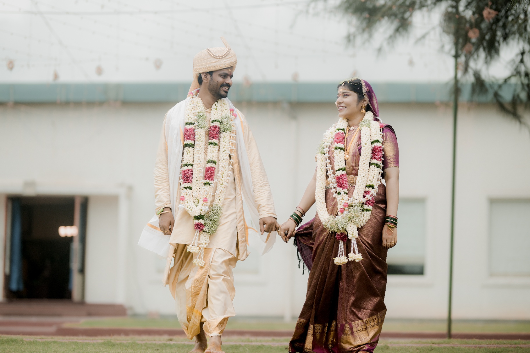 Newlywed couple in traditional attire walking hand in hand on a lawn