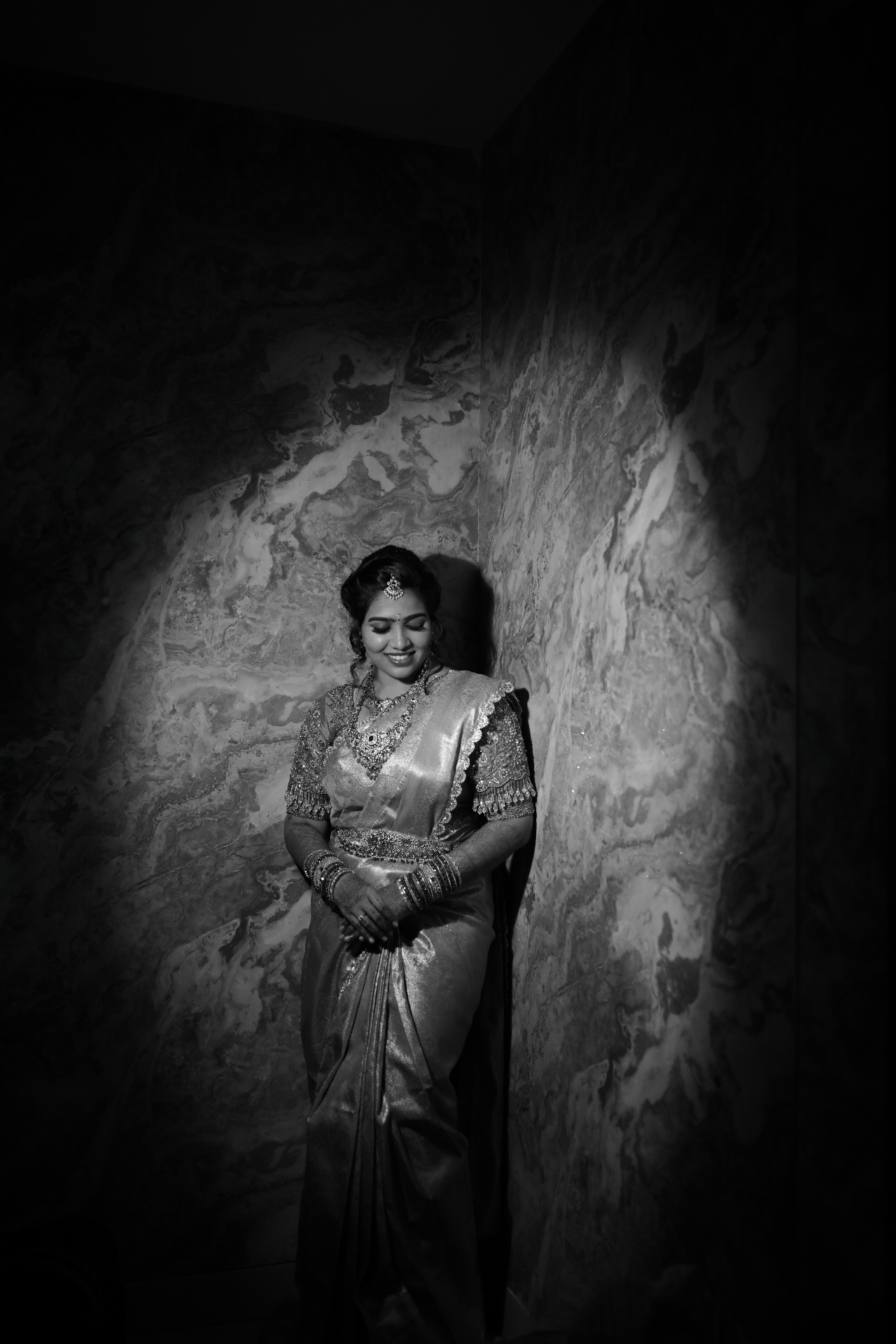 Bride in a silver saree posing against a marble wall in monochrome